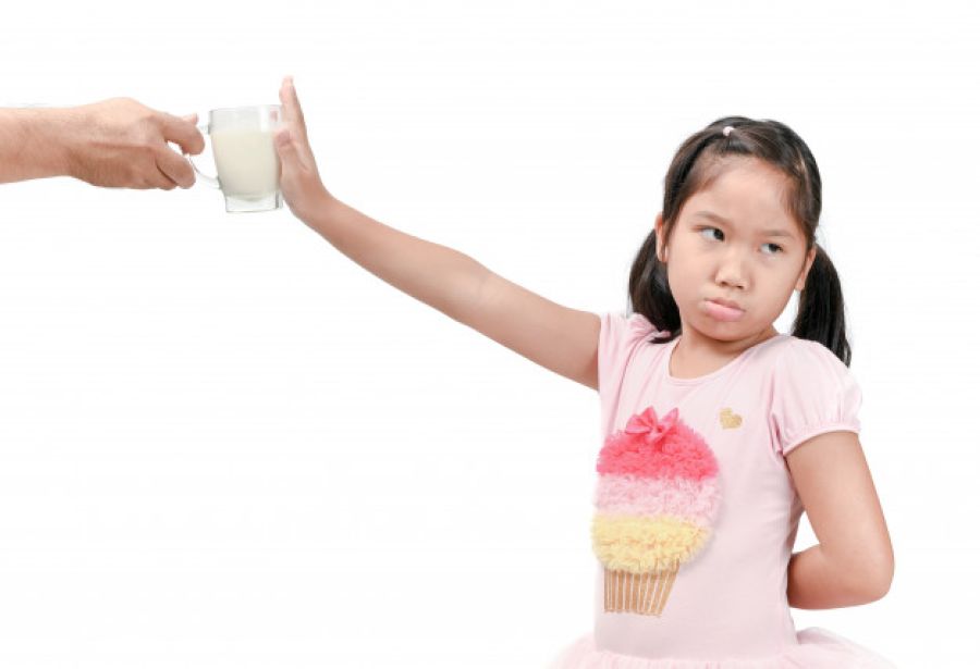 Petite fille refusant de boire un verre de lait (lactose).